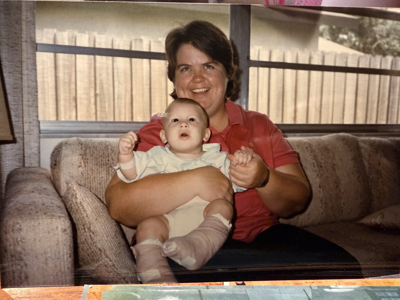 Baby with both lower legs in plaster casts, held on a sofa by a family member