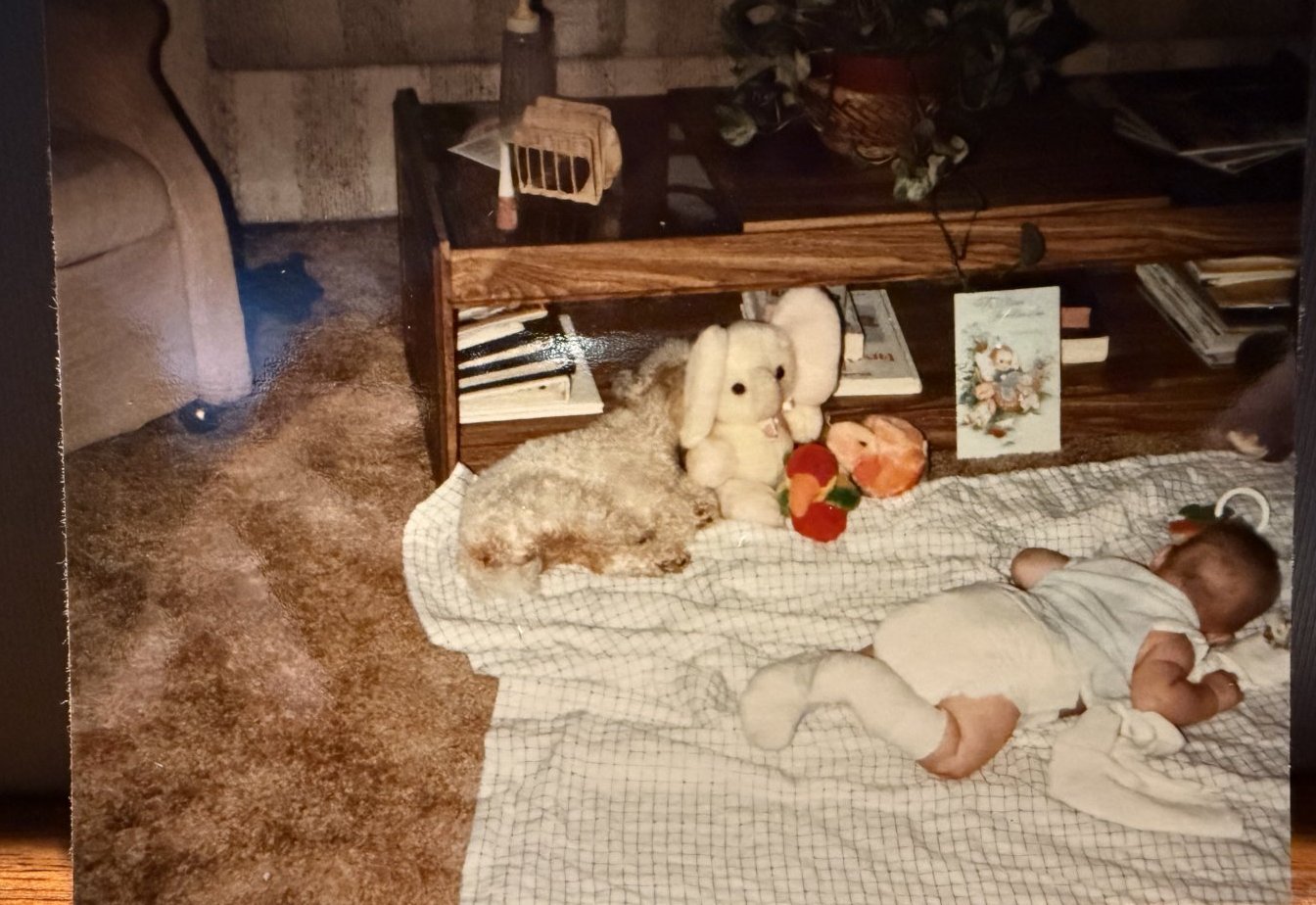 Baby lying on a blanket on the floor with a cast on the leg, a stuffed toy alongside