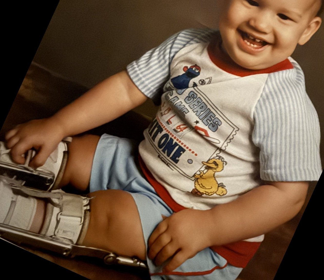 Smiling toddler sitting on the floor, white shoes on metal uprights strapped up both lower legs