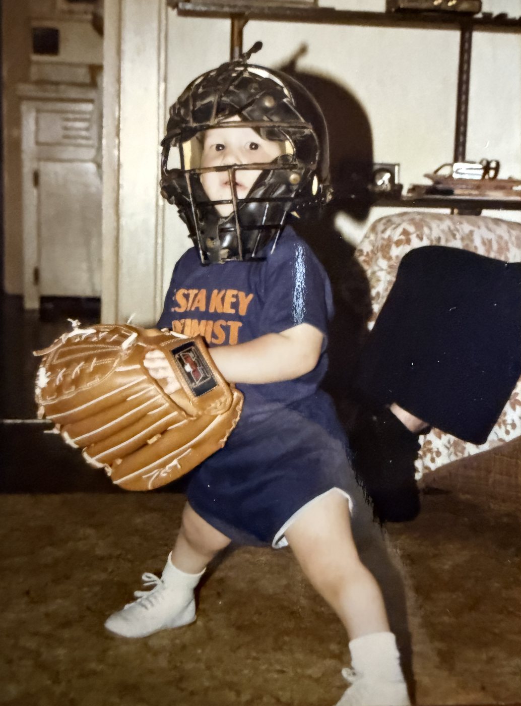 Toddler Heath in a catcher's mask with a baseball glove almost as big as he is