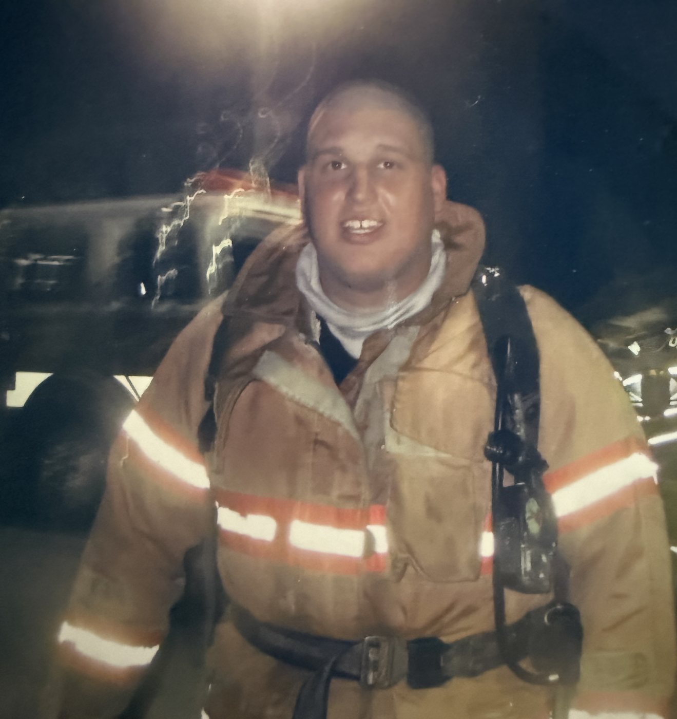 Heath in a firefighter turnout coat and harness, at night