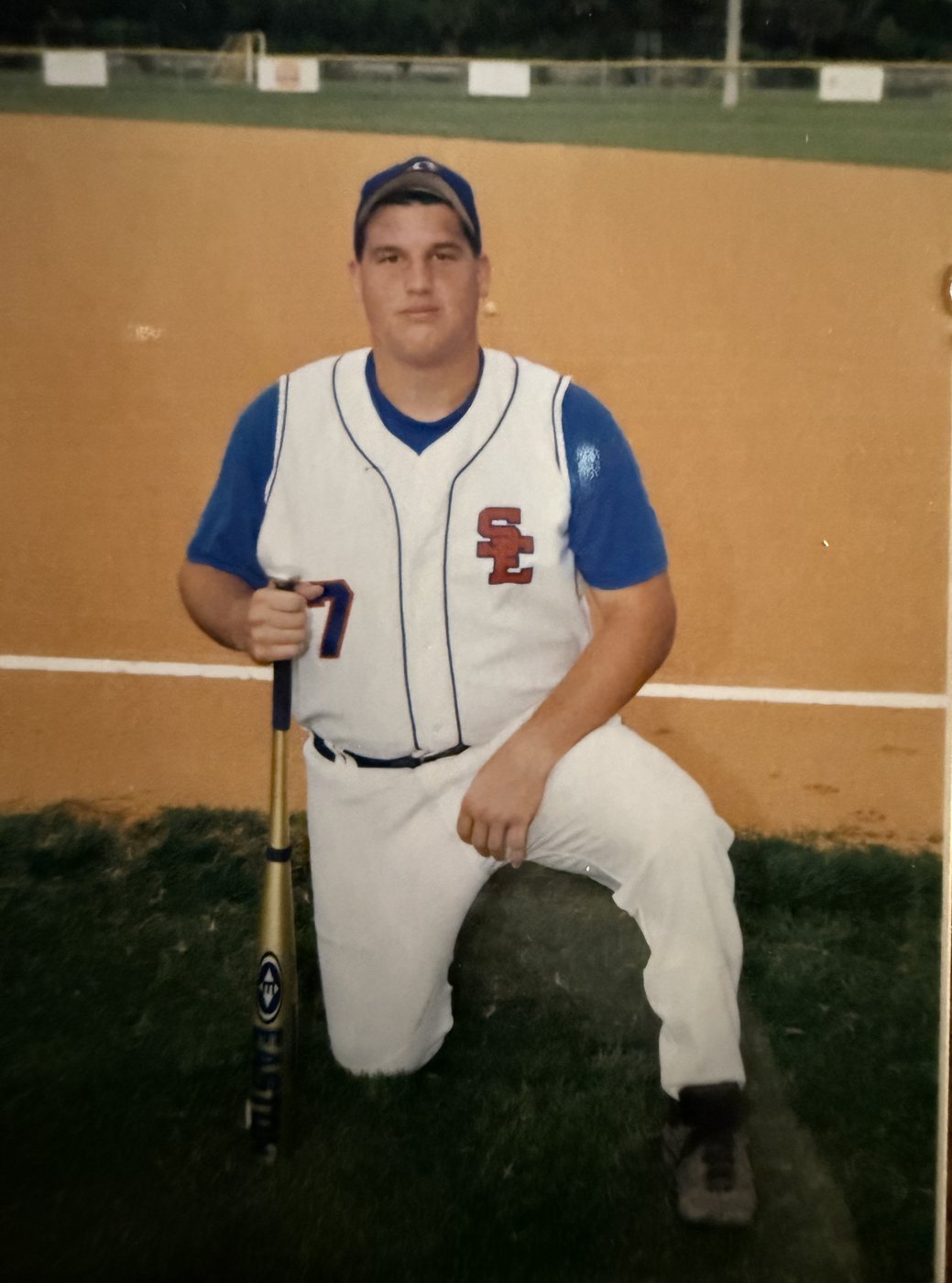 Heath in a high school baseball uniform around 2002, kneeling with a bat, after his triple arthrodesis
