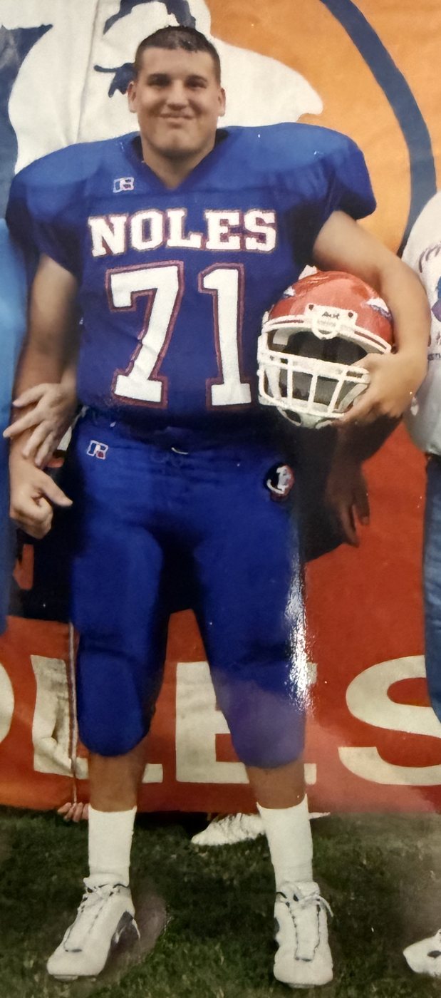 Heath in his high school football uniform, number 71, holding his helmet, October 2000