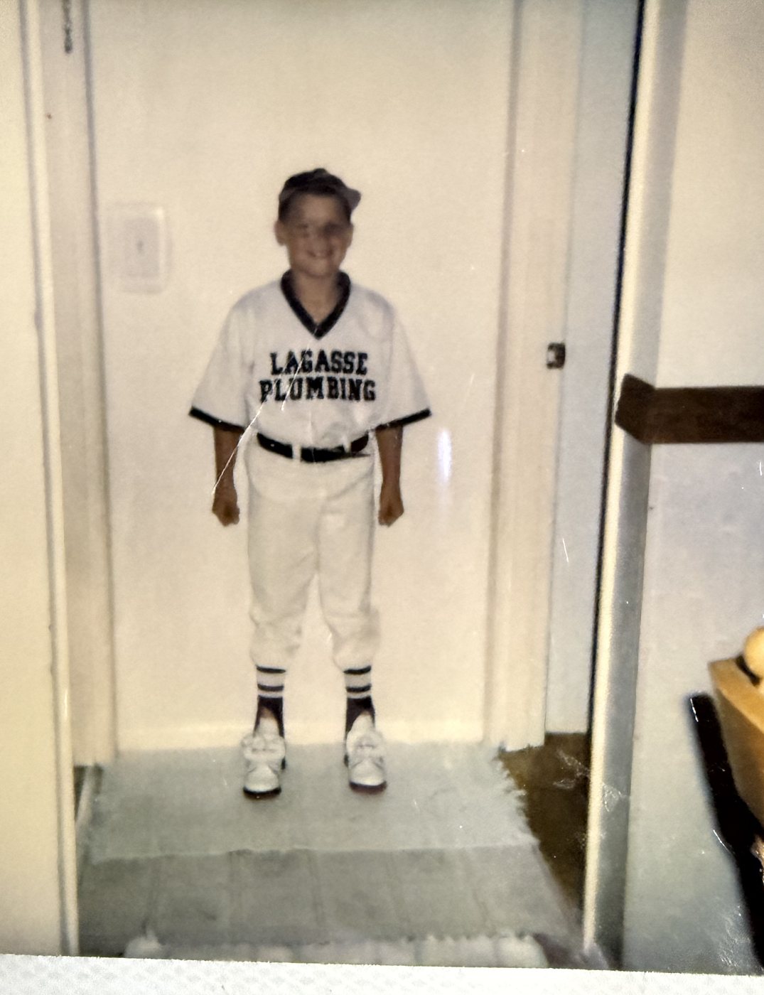 Young Heath in a little league uniform standing in a doorway