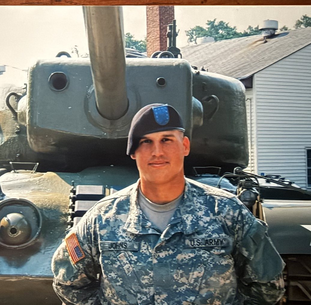 Heath in US Army uniform and beret, standing in front of a tank
