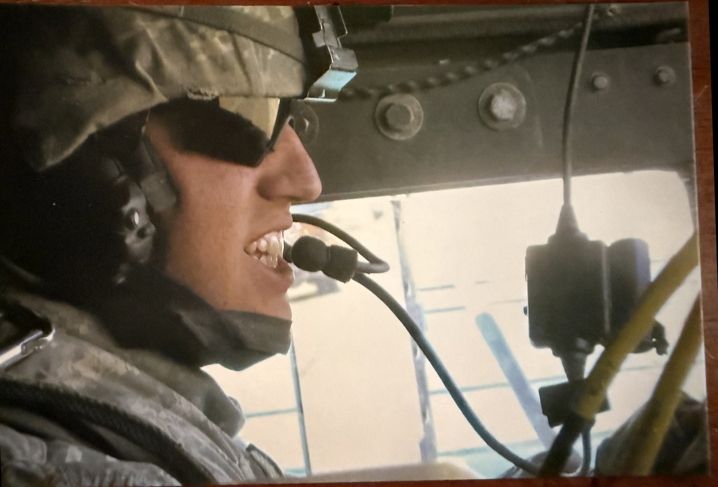 Soldier in combat uniform and helmet with a headset, seated inside a vehicle